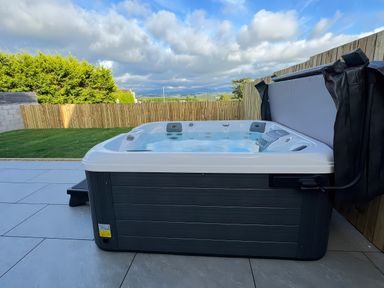 A hot tub on a patio with grass and a fence at 15 Llys Tegeirian in Llangristiolus near Llangefni