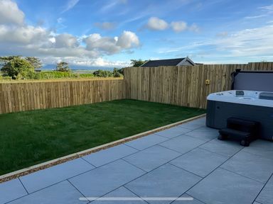 A garden with a hot tub and paved area at 15 Llys Tegeirian near Llangristiolus