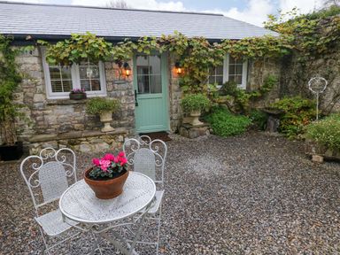 A stone house with a green door and windows with white frames a white metal table and chairs with a flower pot on the table at Little Cloud in Nash near Cowbridge