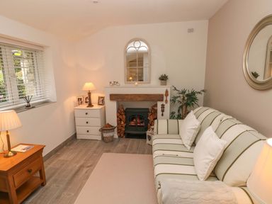 A sitting room with a striped sofa wooden side tables and a fireplace at Little Cloud in Nash near Cowbridge