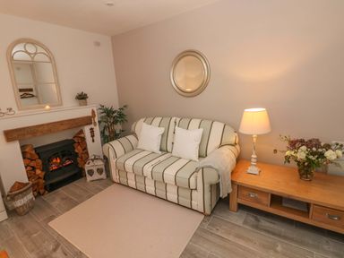 A living room with a striped sofa two white pillows a wooden table lamp flowers a fireplace and a mirror at Little Cloud in Nash near Cowbridge