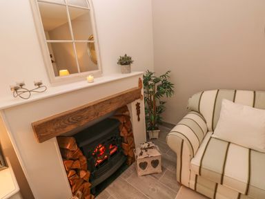 A corner of a room with a fireplace filled with firewood a striped sofa a plant and a mirror on the wall at Little Cloud Nash near Cowbridge