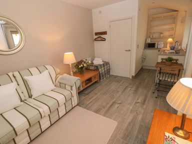 A living area with a striped sofa small wooden tables lamps and a kitchenette at Little Cloud in Nash near Cowbridge