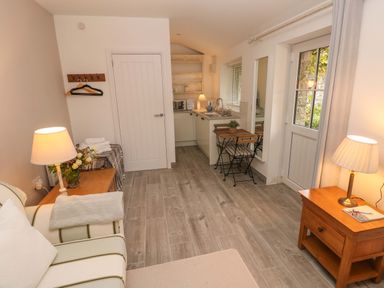 A small living area with a sofa table lamps a kitchenette and a door at Little Cloud in Nash near Cowbridge