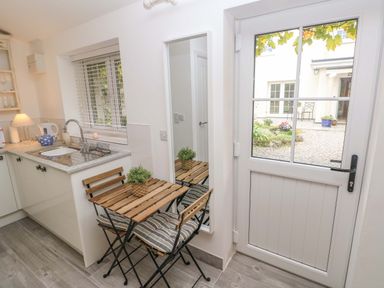 A kitchen with a wooden table and two chairs near a sink and a glass door showing a garden at Little Cloud Nash near Cowbridge