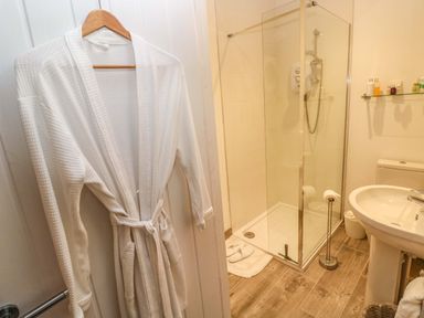 A bathroom with a white bathrobe hanging on a door a shower with glass enclosure a sink toilet and toiletries on a shelf at Little Cloud Nash near Cowbridge