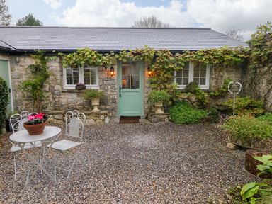 A stone cottage with a green door surrounded by plants and a gravel courtyard with a metal table and chairs at Little Cloud Nash near Cowbridge