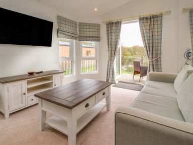 A living room with a sofa a coffee table a TV on a stand and windows with plaid curtains at Lakeview Lodge in Forton near Garstang