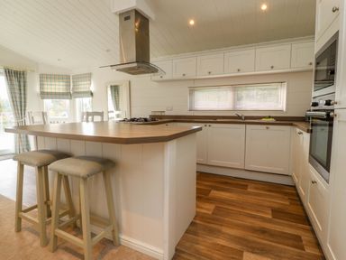 A kitchen with an island and stools a stove and oven with plaid curtains at Lakeview Lodge in Forton near Garstang