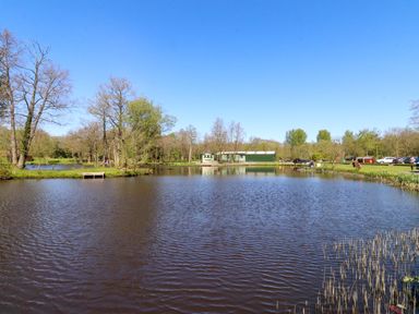 A scenic view of a pond with trees and a building at Lakeview Lodge in Forton near Garstang