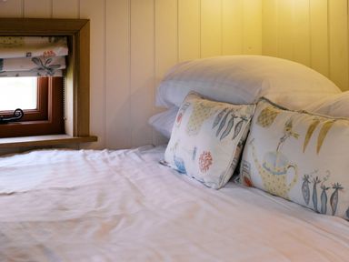 A bed with pillows and a window at Bonnie's Shepherds Hut at Shepherds Lodge Retreat and Wellness, Bottesford near Redmile and Vale of Belvoir