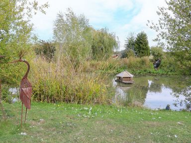 A pond with a decorative house and metal sculpture at Lillie's Shepherds Hut at Shepherds Lodge Retreat and Wellness Bottesford near Redmile and Vale of Belvoir