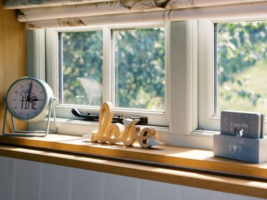 A kitchen window with a clock and decorative items at Herbie's Shepherds Hut at Shepherds Lodge Retreat and Wellness Bottesford near Redmile and Vale of Belvoir