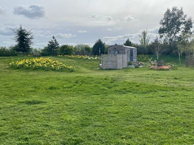 A garden with a shepherd's hut, flowers, and trees at Herbie's Shepherds Hut at Shepherds Lodge Retreat and Wellness Bottesford near Redmile and Vale of Belvoir