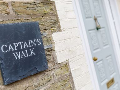 A stone and brick wall with a black plaque reading Captains Walk next to a pale blue door at Captains Walk Newquay