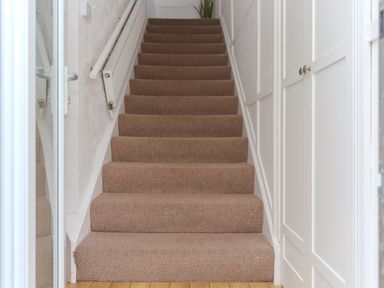 A carpeted staircase with white walls a radiator on the left and white cabinets on the right at Captains Walk in Newquay