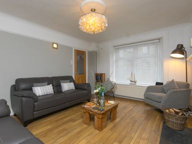 A living room with two gray sofas a small wooden table with wine glasses and snacks and a window with blinds at Captain's Walk in Newquay