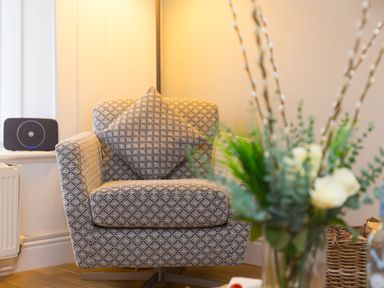 A patterned armchair with a matching cushion next to a window and a vase of flowers in the foreground at Captain's Walk in Newquay
