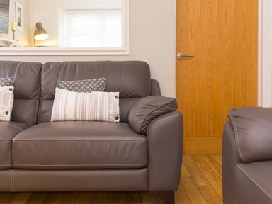 A living room with a brown leather sofa and a wooden door at Captain's Walk in Newquay