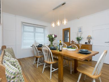 A dining room with a wooden table set with plates glasses and bottles surrounded by chairs and a bench at Captains Walk in Newquay