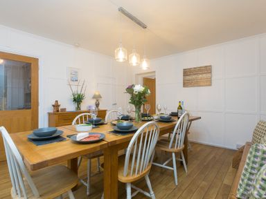 A dining room with a wooden table set with plates glasses and bowls surrounded by white chairs at Captain's Walk in Newquay