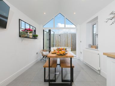 A dining area with a wooden table and benches open to a fenced outdoor space at Captain's Walk in Newquay