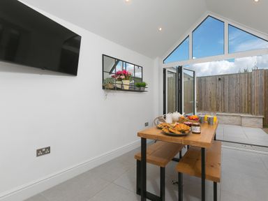 A dining area with a wooden table and benches set with breakfast items and open glass doors to a fenced outdoor patio at Captain's Walk in Newquay
