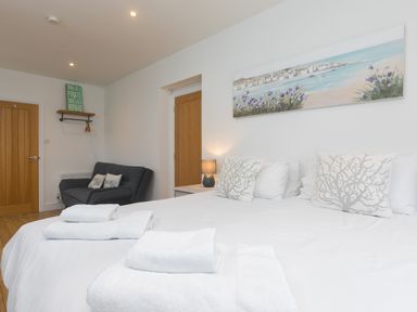 A bedroom with a large bed a grey sofa two wooden doors and a wall painting at Captain's Walk in Newquay