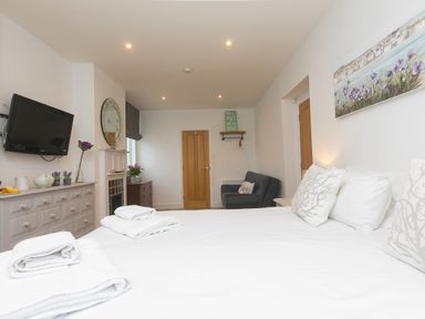 A bedroom with a bed with folded towels a television on the wall and a gray chair at Captain's Walk in Newquay