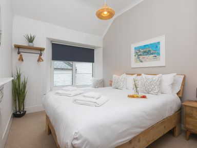 A bedroom with a bed with white linens and patterned pillows next to a window with a dark blind and plants at Captains Walk in Newquay