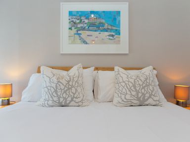 A bed with white and patterned pillows and two bedside tables with lamps and a framed picture above the bed at Captains Walk in Newquay