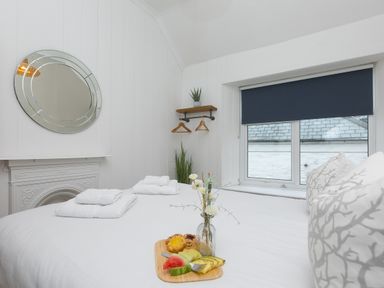 A bedroom with white bedding towels on bed window with dark blind and round mirror on wall at Captain's Walk in Newquay