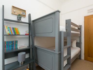 A bedroom with a grey bunk bed and a grey ladder shelf holding books and a lamp at Captain's Walk in Newquay