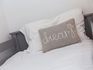 A bed with white sheets and pillows and a gray cushion with the word dream at Captain's Walk in Newquay