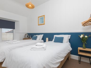 A bedroom with two single beds with white bedding and blue cushions at Captain's Walk in Newquay