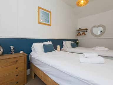 A bedroom with two single beds a wooden chest of drawers and a heart shaped mirror at Captains Walk in Newquay