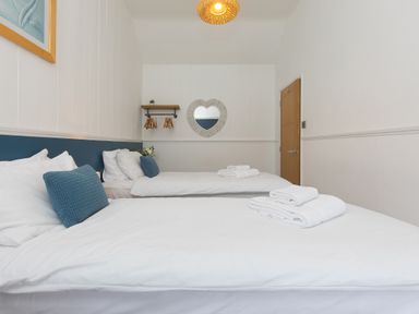 A bedroom with two single beds white bedding blue pillows a heart shaped mirror and a wooden door at Captains Walk in Newquay