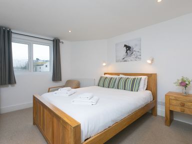 A bedroom with a wooden bed with white bedding and striped pillows next to a wooden nightstand with flowers at Captains Walk in Newquay
