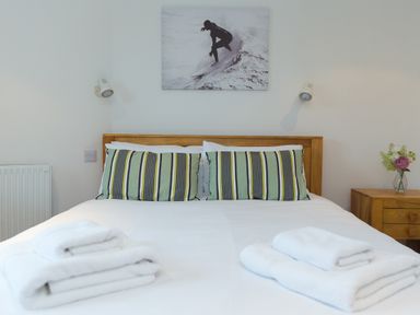 A bed with striped pillows and folded towels with a wooden bedside table and a black and white surfer picture at Captain's Walk in Newquay