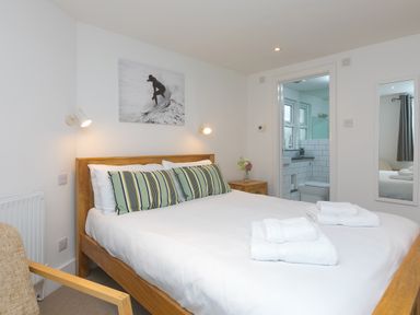 A bedroom with a wooden bed white bedding striped pillows towels bedside table and an en suite bathroom at Captain's Walk in Newquay