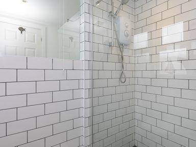 A tiled shower area with a wall-mounted shower unit and a glass partition in a bathroom at Captain's Walk in Newquay