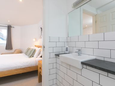 A bedroom with a bed and a chair next to a bathroom sink and mirror at Captains Walk in Newquay