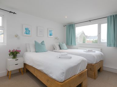 A bedroom with two single beds bedside table with flowers and framed pictures at Captain's Walk in Newquay