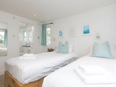 A bedroom with two single beds white bedding blue pillows and a view of a bathroom at Captain's Walk in Newquay