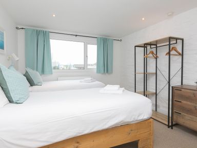 A bedroom with two beds pillows folded towels open closet with hangers and chest of drawers at Captains Walk in Newquay