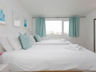 A bedroom with two beds white bedding and blue pillows under a window with blue curtains at Captain's Walk in Newquay