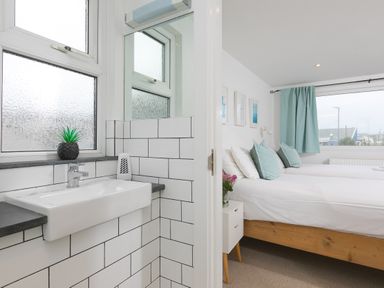 A bathroom sink with a plant and a bedroom with two beds and blue cushions at Captains Walk in Newquay