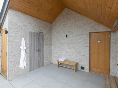 A shower area with a wooden bench and a white robe hanging on the wall at Captains Walk in Newquay