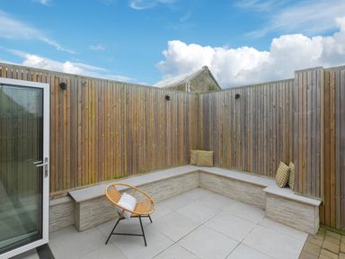 A small outdoor patio with a corner bench and a single chair surrounded by wooden fencing at Captain's Walk in Newquay