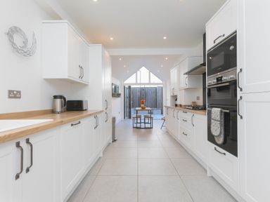 A kitchen with white cabinets wooden countertops and a dining table at Captains Walk in Newquay